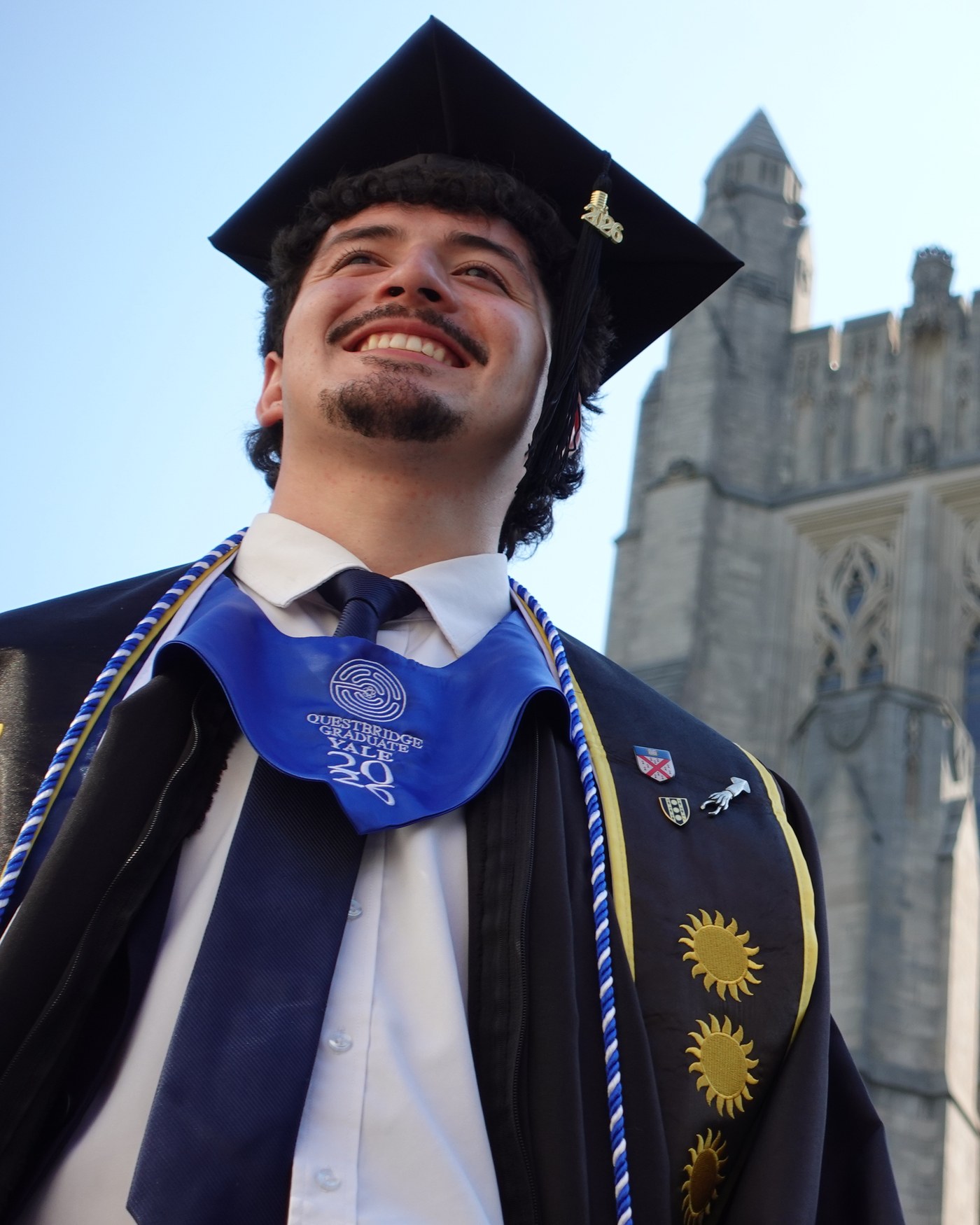 Nico Ramos in his graduation cap and gown in front of a Yale tower